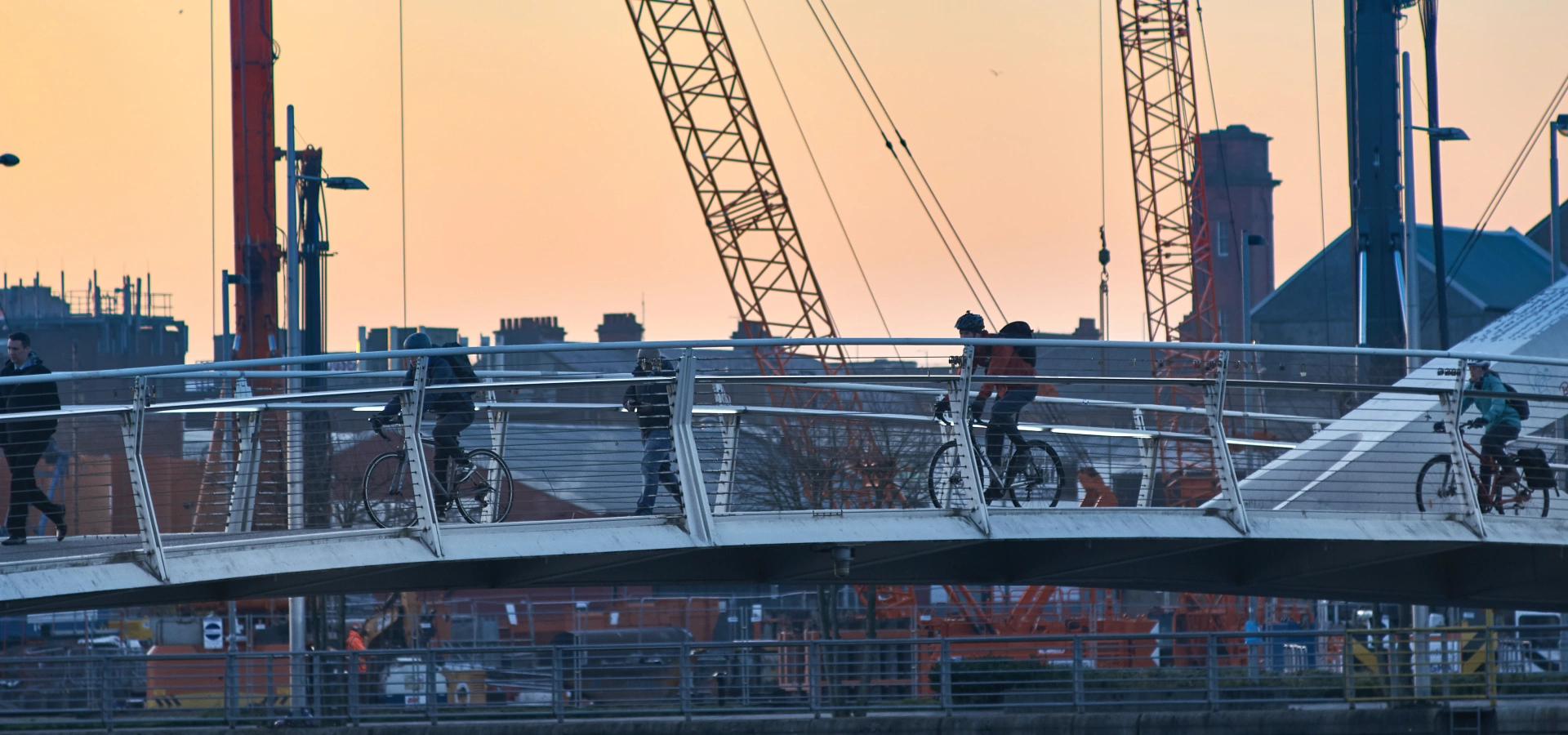 People cycling on a Glasgow bridge at dawn.