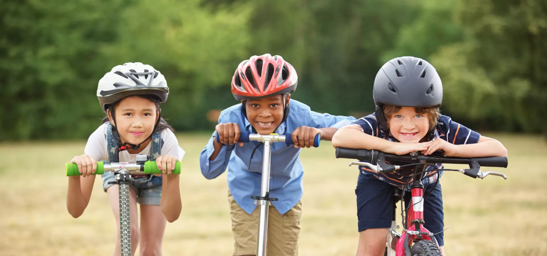 Two children on their scooters and one on their bike, all smiling and looking straight at the camera.