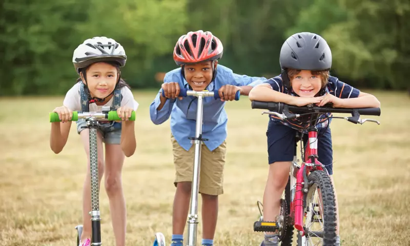 Two children on their scooters and one on their bike, all smiling and looking straight at the camera.