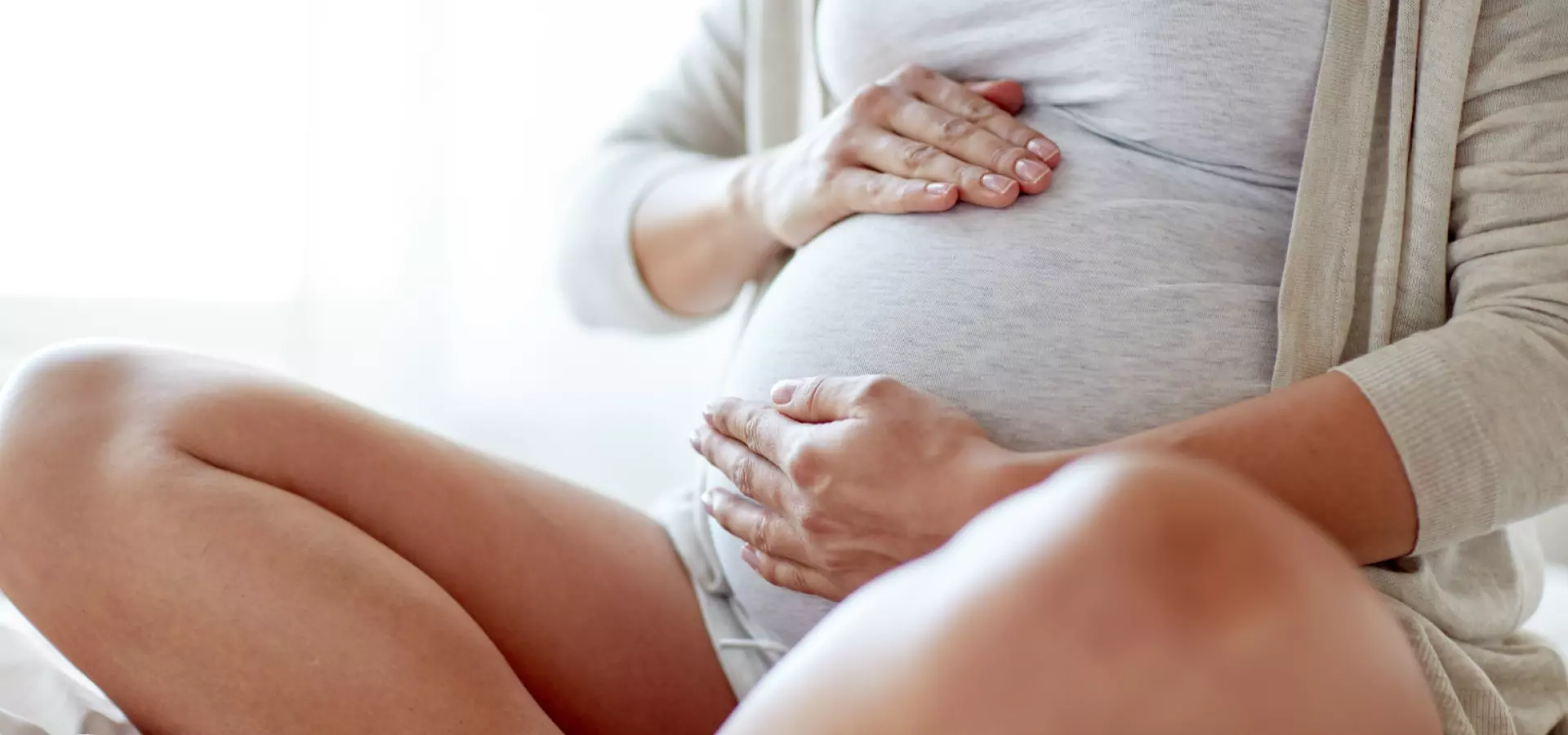 Cropped image of a woman sitting down and holding her pregnant belly.