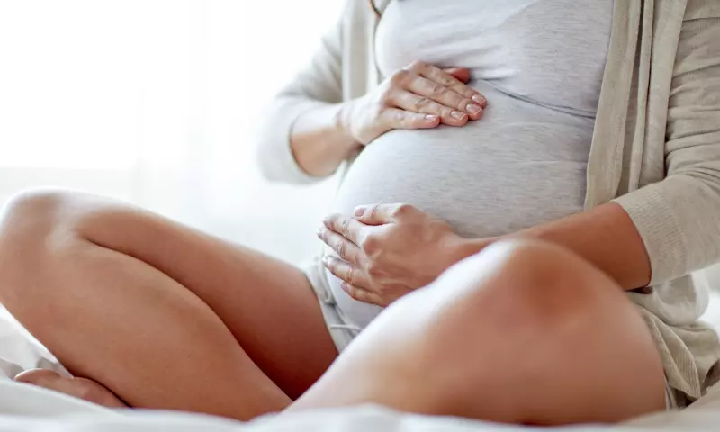 Cropped image of a woman sitting down and holding her pregnant belly.