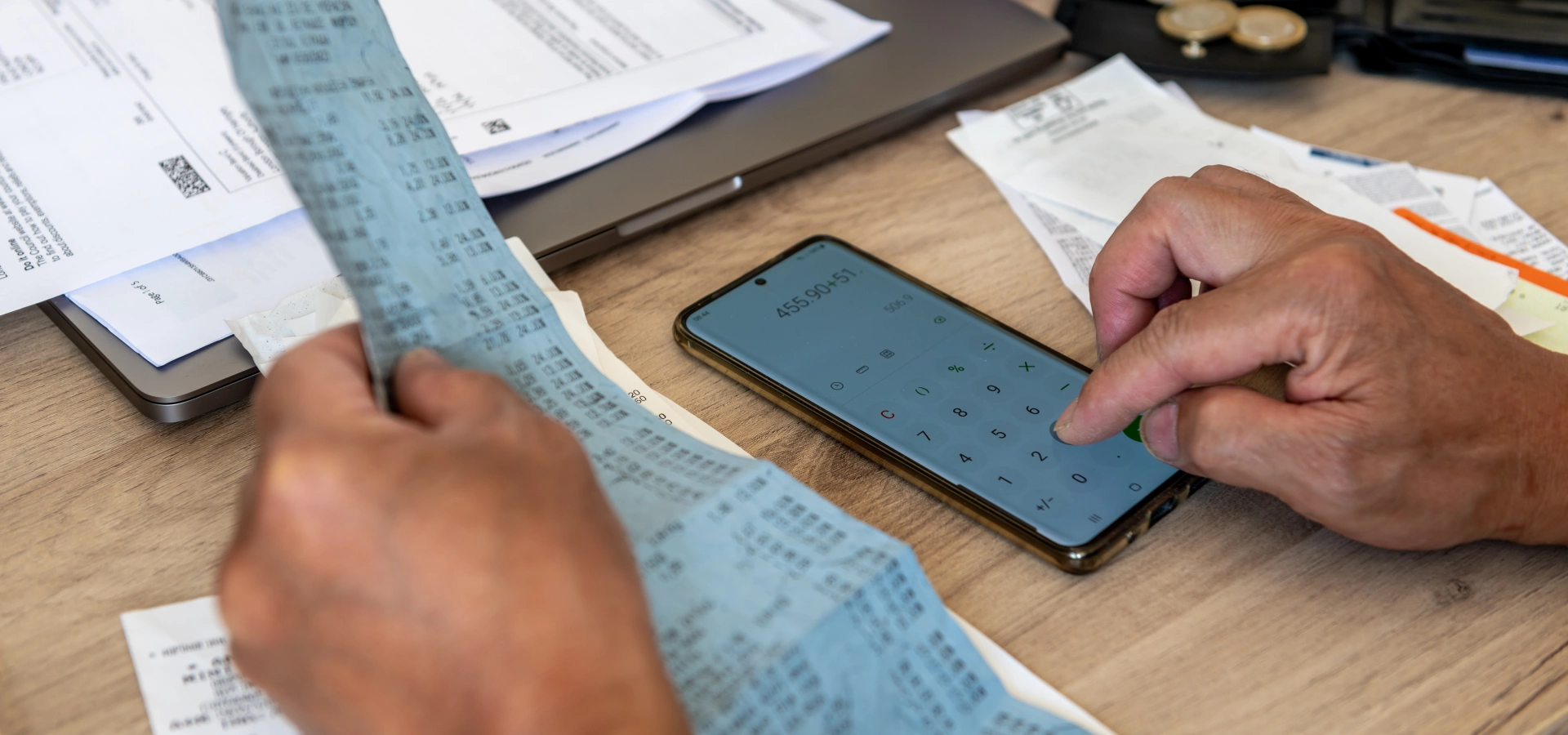 A person at a desk, adding amounts from bills and receipts. There are some coins and notes on the desk.