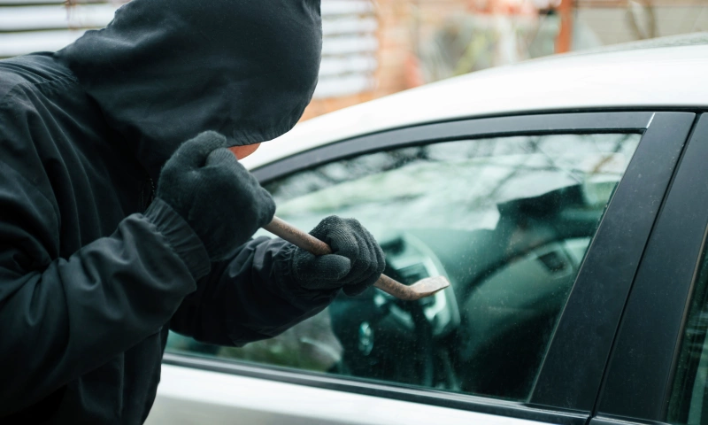 Somebody in a black hoodie and black gloves stealing a car.