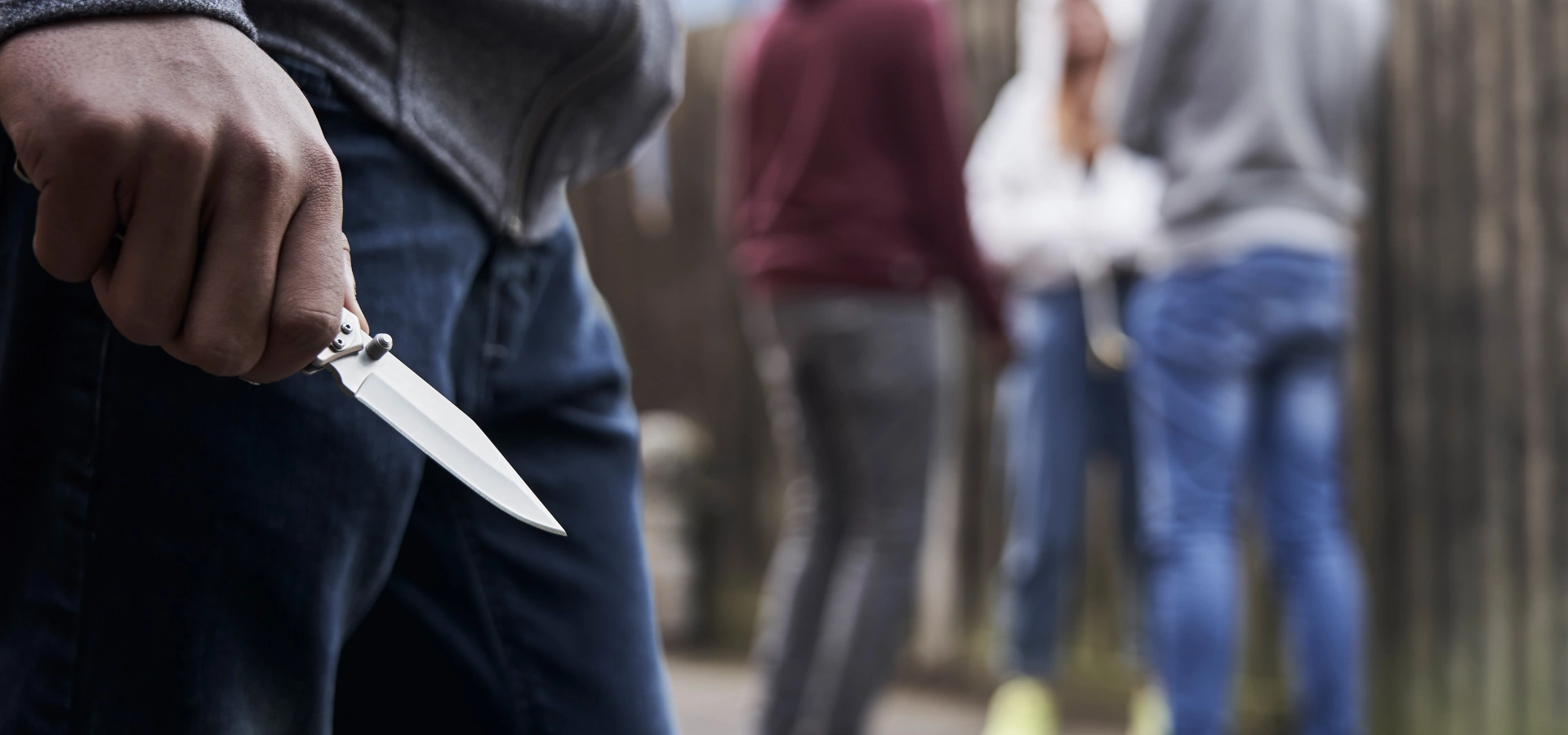 Someone holding a knife angrily, with a group of people blurred in the background.