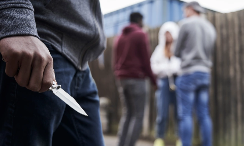 Someone holding a knife angrily, with a group of people blurred in the background.