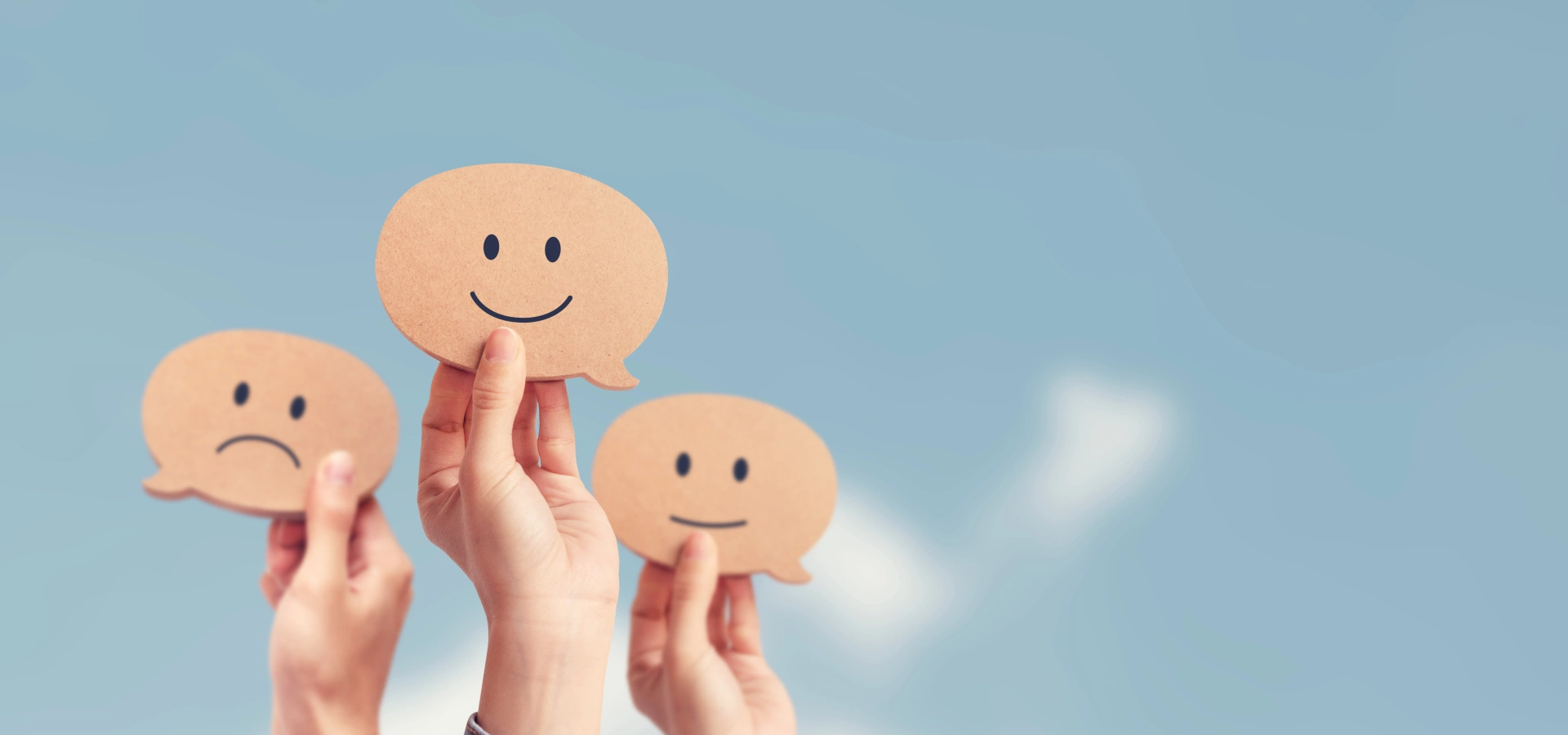 Three hands, each holding a cardboard cut-out of a smiley or sad face.