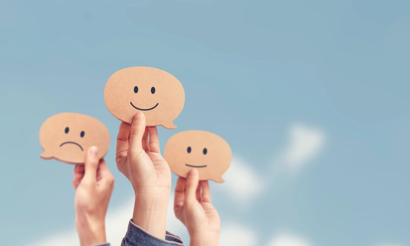 Three hands, each holding a cardboard cut-out of a smiley or sad face.