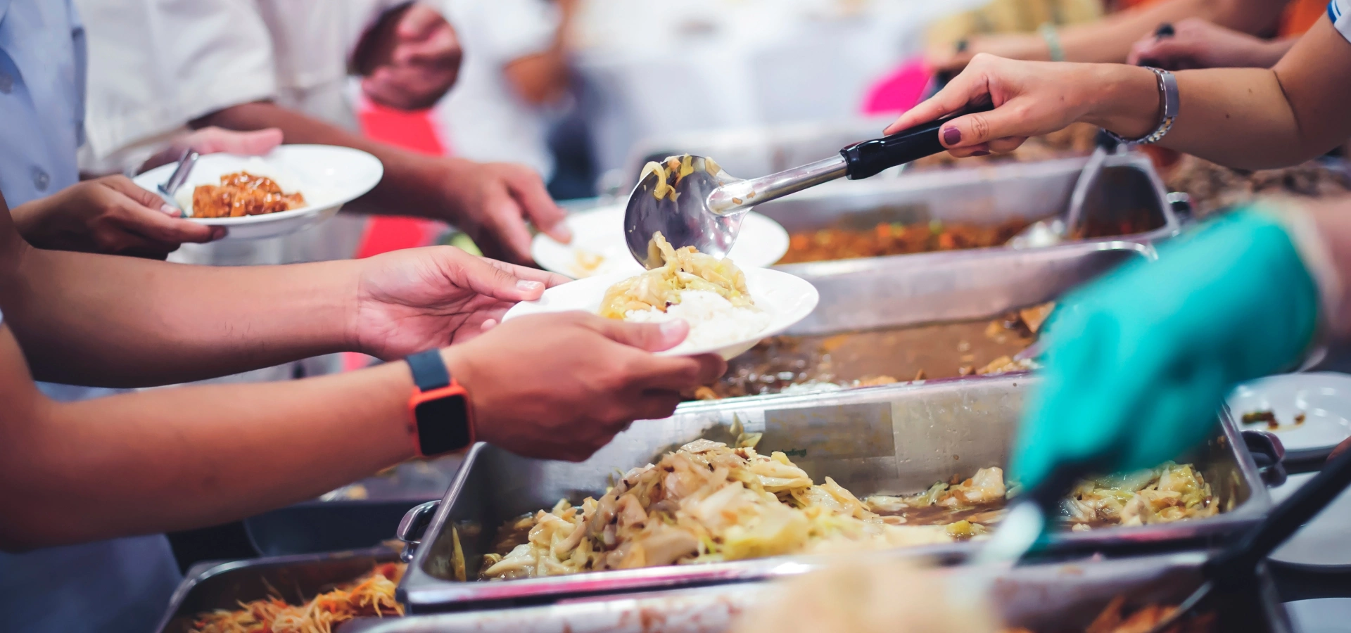 Large dishes filled with food, with people filling plates.