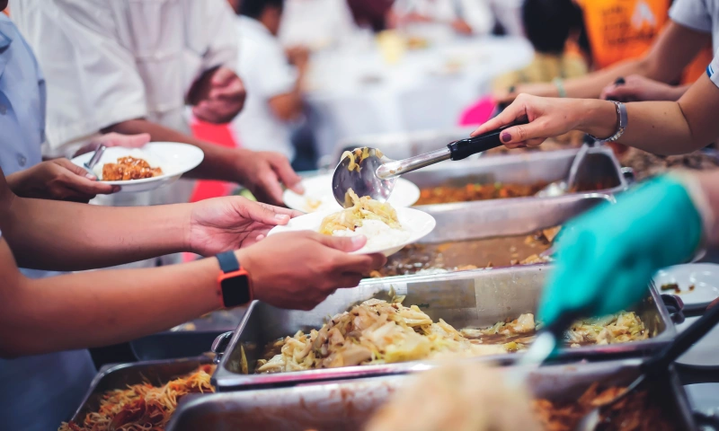 Large dishes filled with food, with people filling plates.