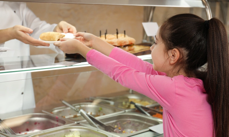 A young girl being handed a plate of food at school.