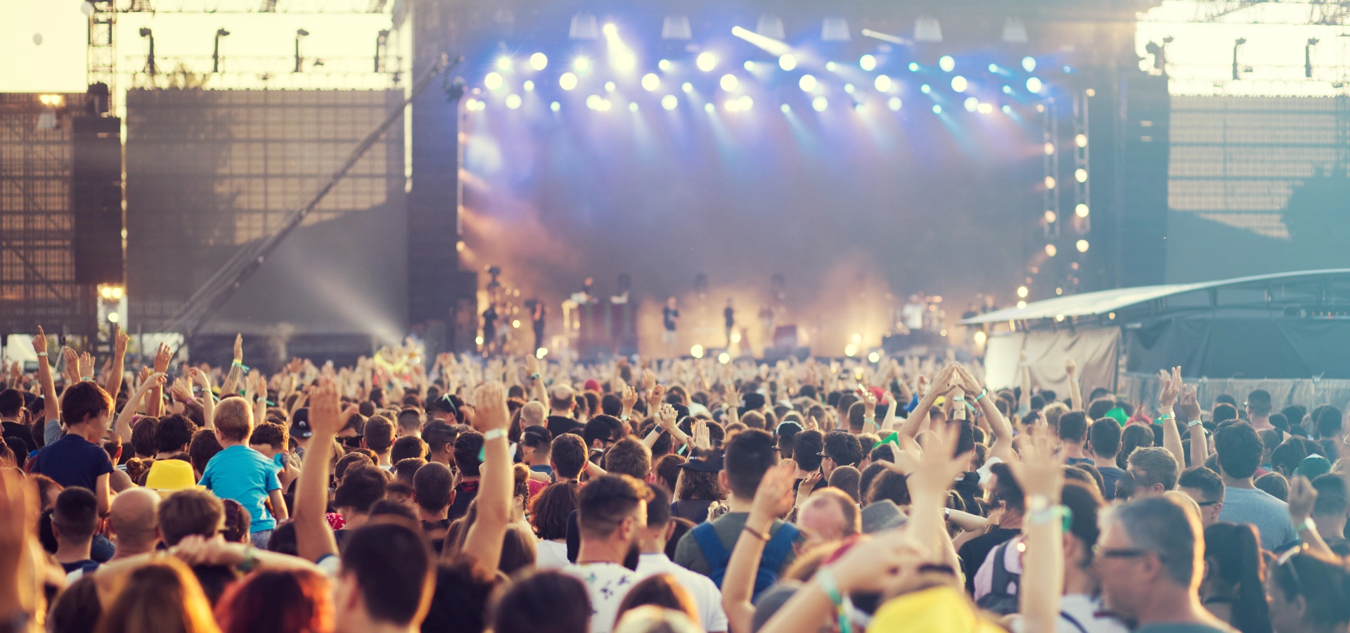 A crowd dancing at a festival, with a stage and big screen in the background.