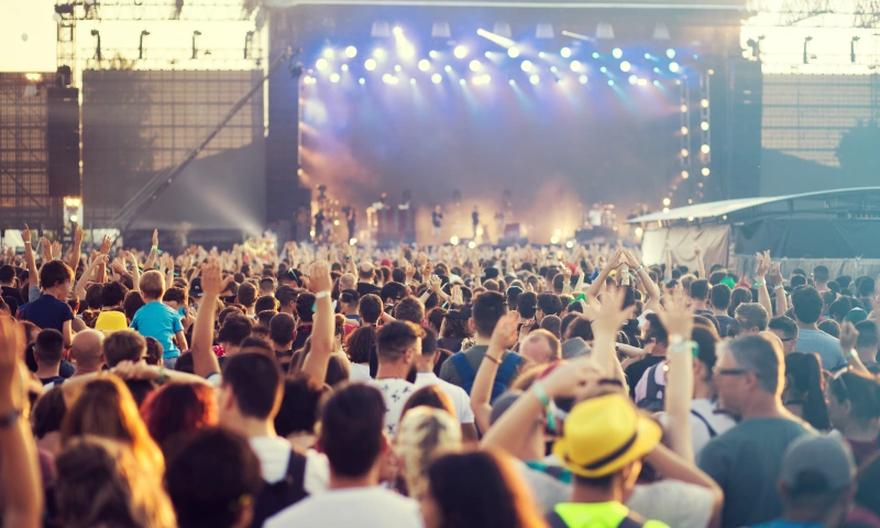 A crowd dancing at a festival, with a stage and big screen in the background.