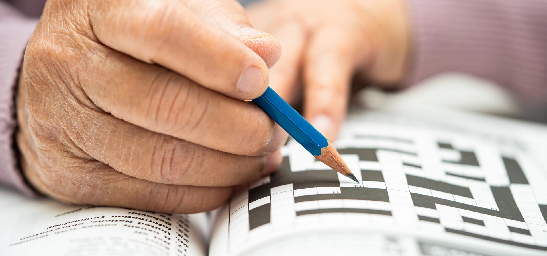 Hand of an older person holding a pen and doing a crossword puzzle.