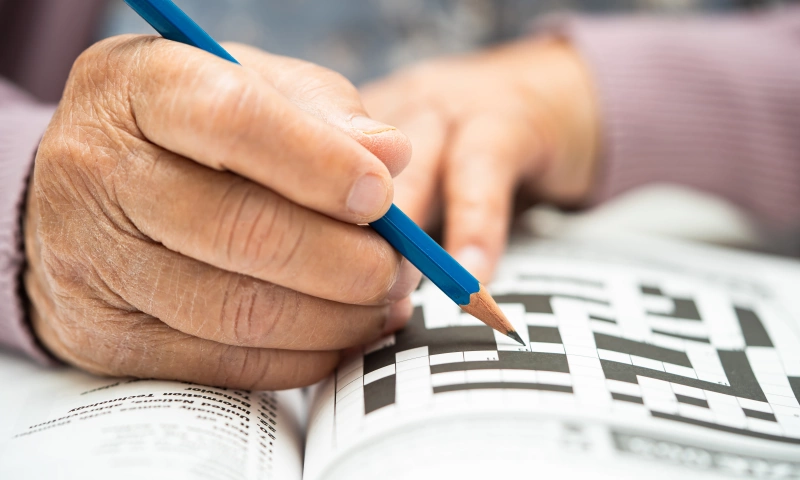 Hand of an older person holding a pen and doing a crossword puzzle.