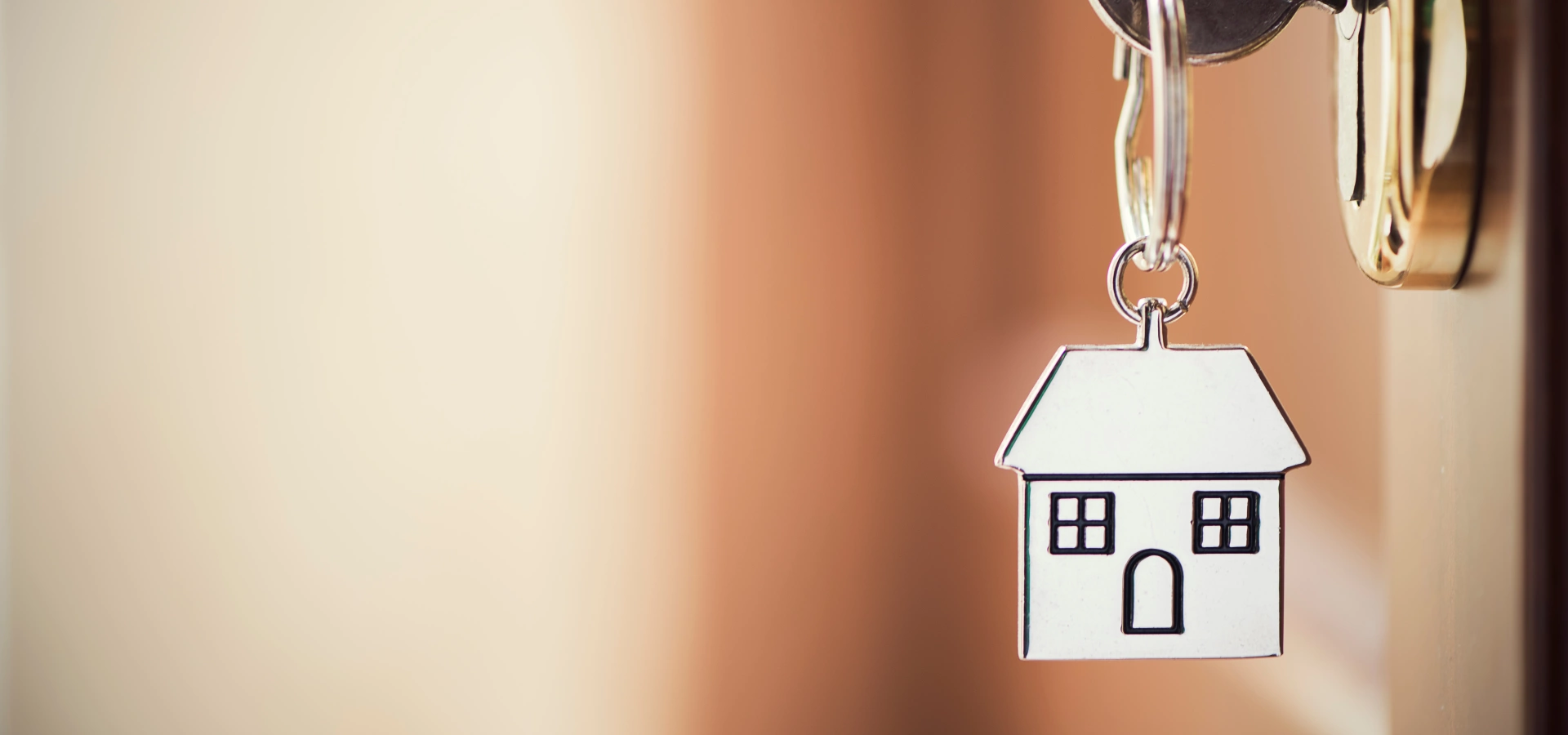 Keys in a door with a keyring shaped as a house.