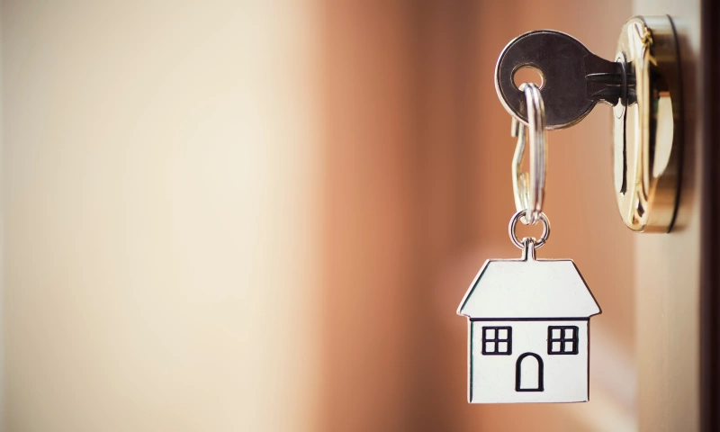 Keys in a door with a keyring shaped as a house.