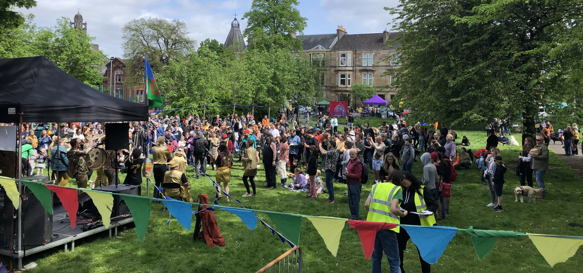 Community event celebrating the Festival of resistance in Kenmure street, Glasgow. There are people and stall as well as bunting in the local park.