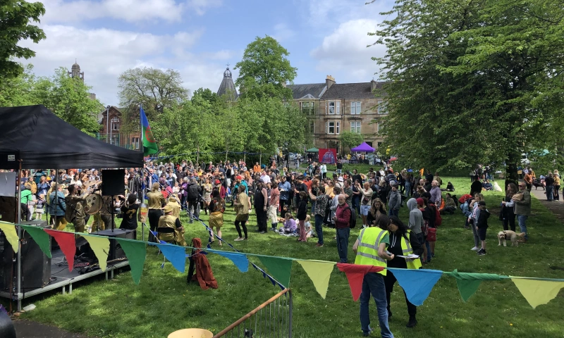 Community event celebrating the Festival of resistance in Kenmure street, Glasgow. There are people and stall as well as bunting in the local park.