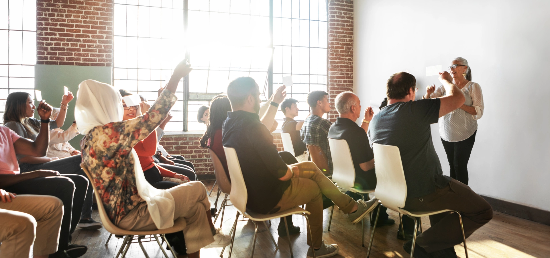 Group of people in a room, some with their hand up, participating in a discussion.