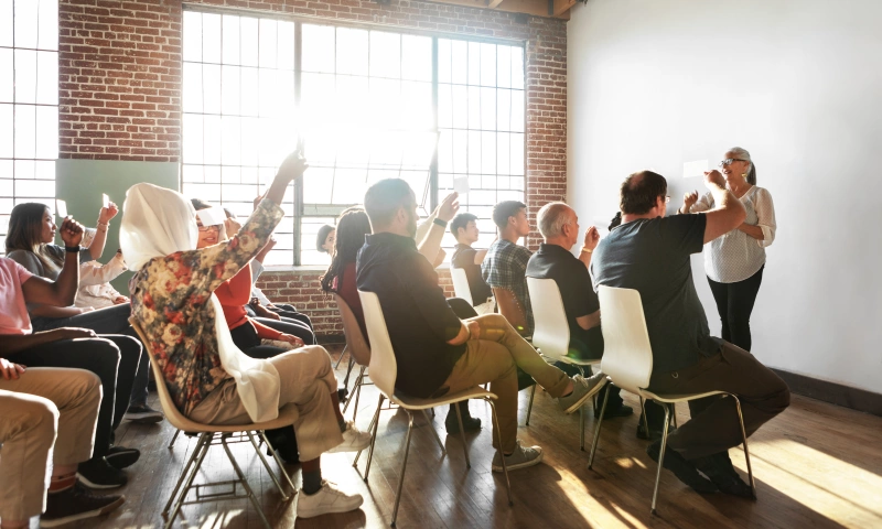 Group of people in a room, some with their hand up, participating in a discussion.