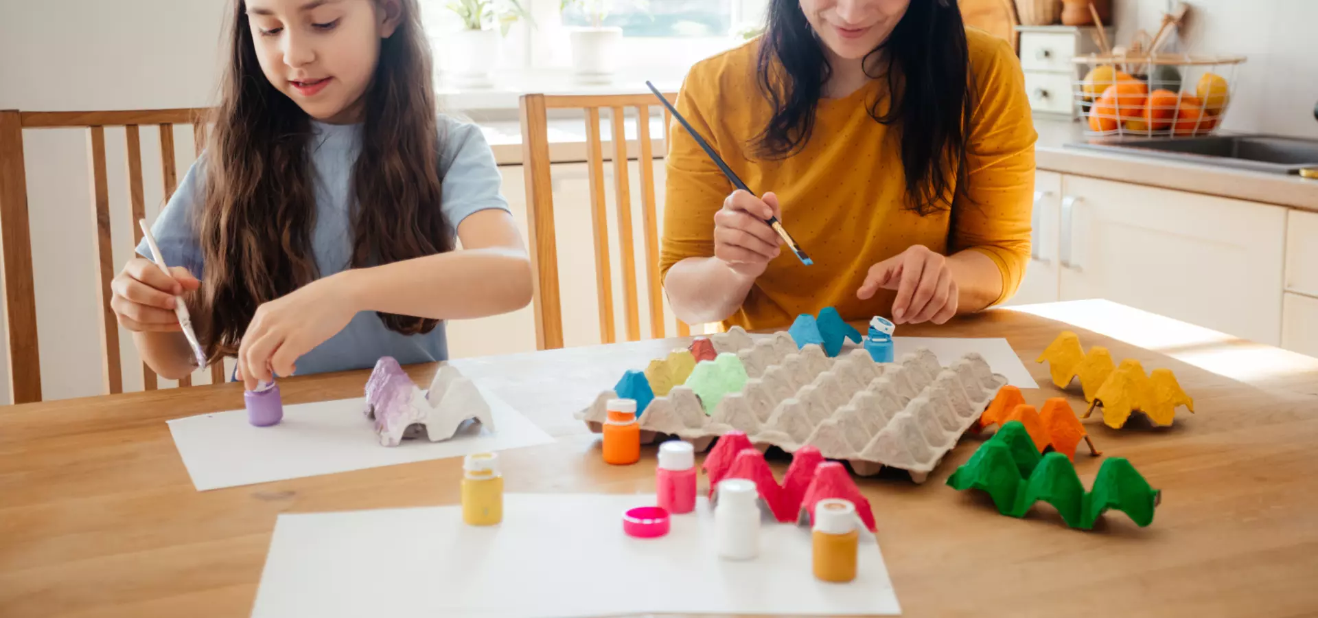 A mother and daughter sitting at the kitchen table and painting egg cartons.