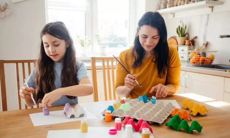 A mother and daughter sitting at the kitchen table and painting egg cartons.