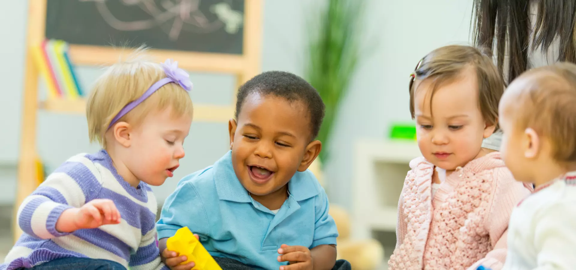 Four toddlers of diverse gender and ethnicity playing together with toys.