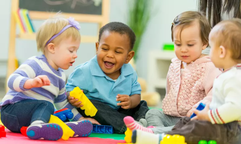 Four toddlers of diverse gender and ethnicity playing together with toys.