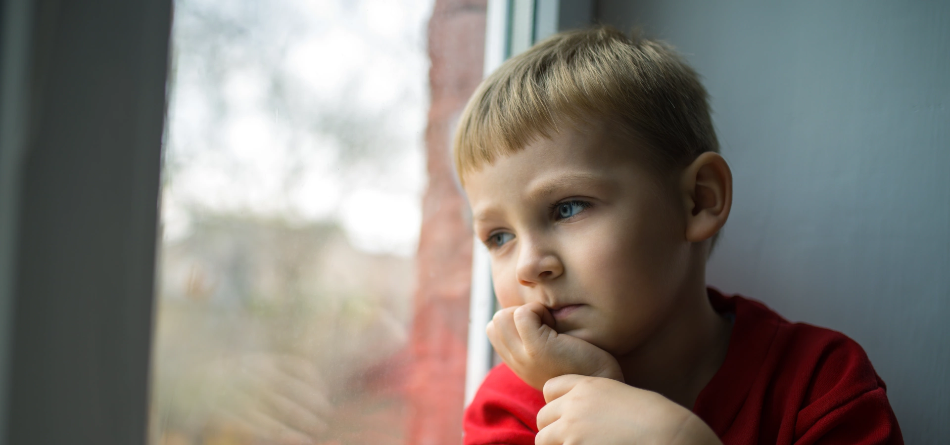 Young boy looking pensively out a window.