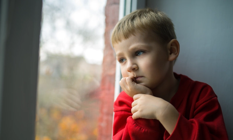 Young boy looking pensively out a window.