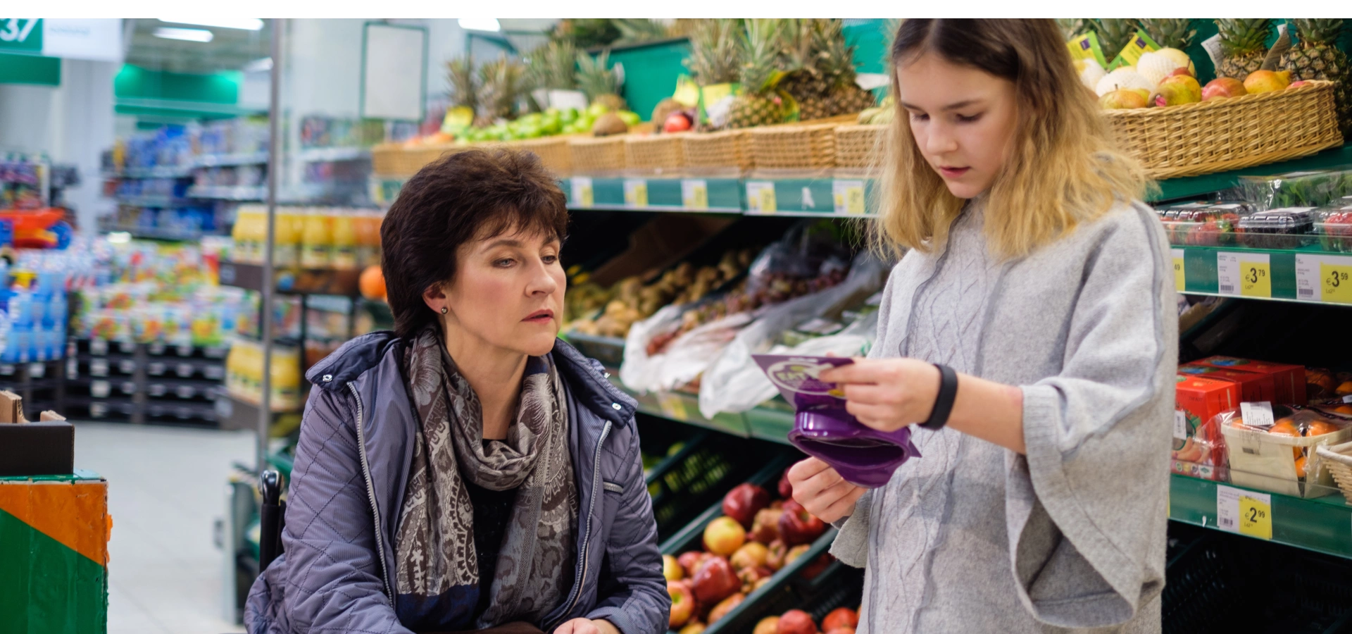 A mother in a wheelchair with her teen daughter, buying groceries from the supermarket.