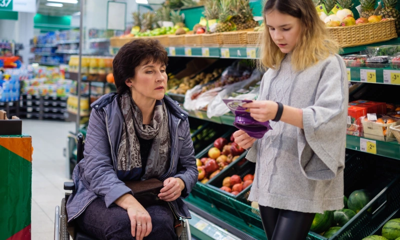 A mother in a wheelchair with her teen daughter, buying groceries from the supermarket.