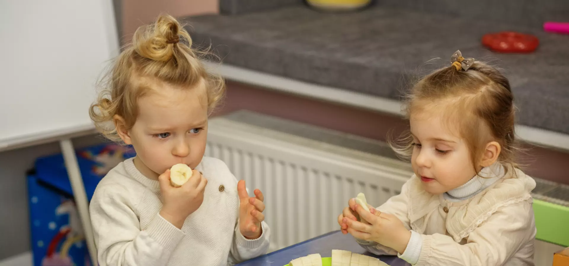 Young siblings eating snacks together, sitting at a kid table.