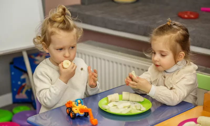 Young siblings eating snacks together, sitting at a kid table.