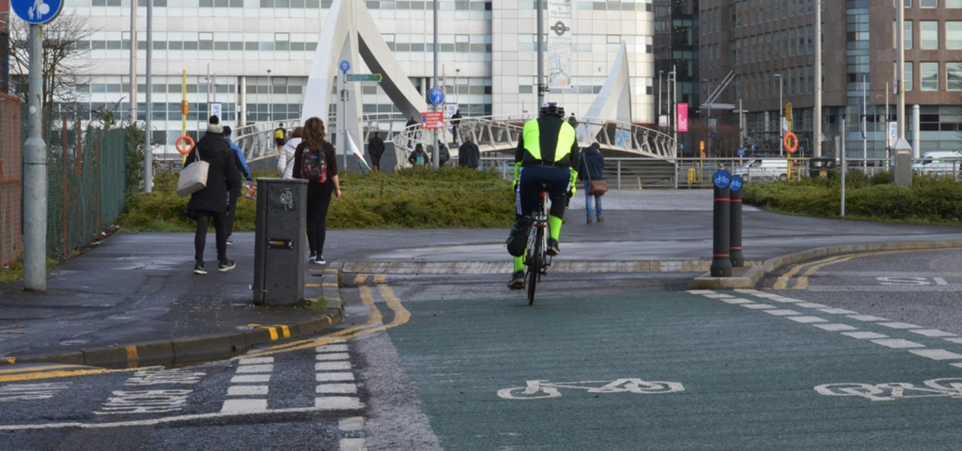 A cyclist on a cycle lane in Glasgow with a pedestrian bridge in the background.