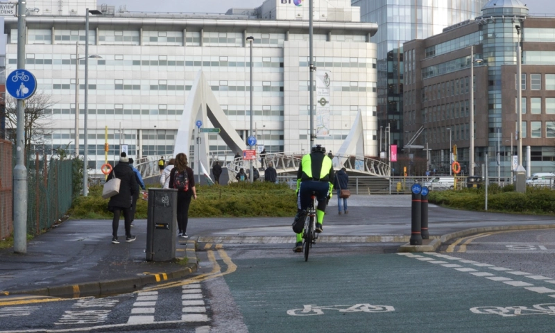 A cyclist on a cycle lane in Glasgow with a pedestrian bridge in the background.