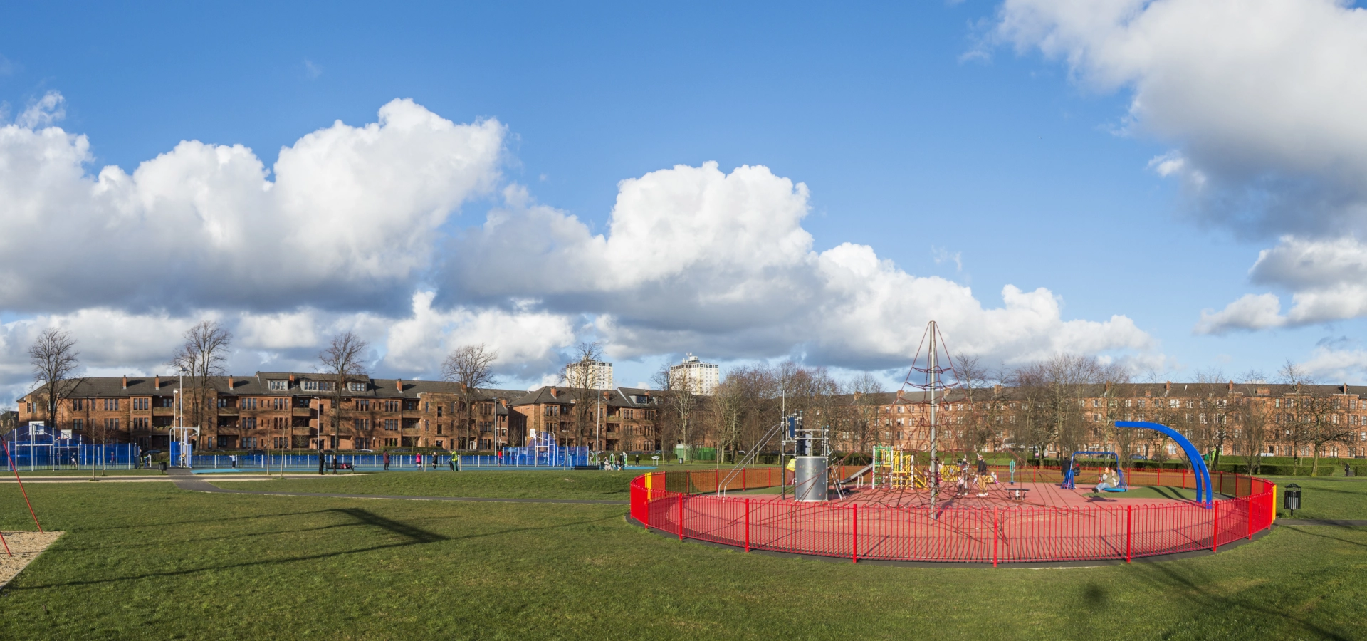 A playpark roundabout with some flats in the background.