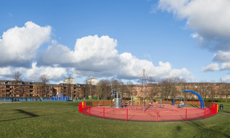 A playpark roundabout with some flats in the background.