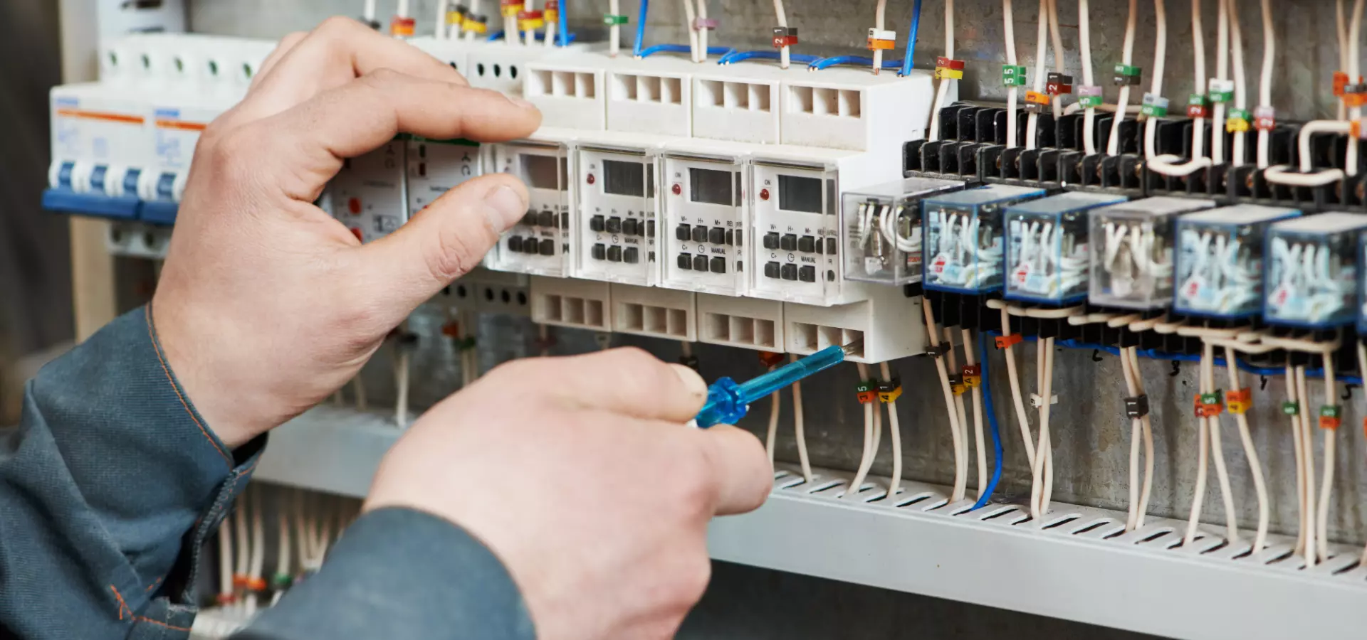 Close up of the hands of an electrician working on a fuse box.