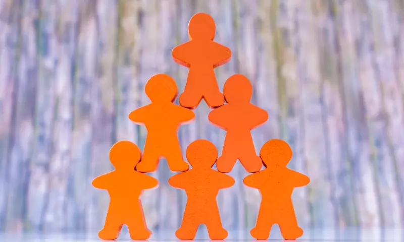 Orange wooden peg people arranged in the shape of a pyramid.