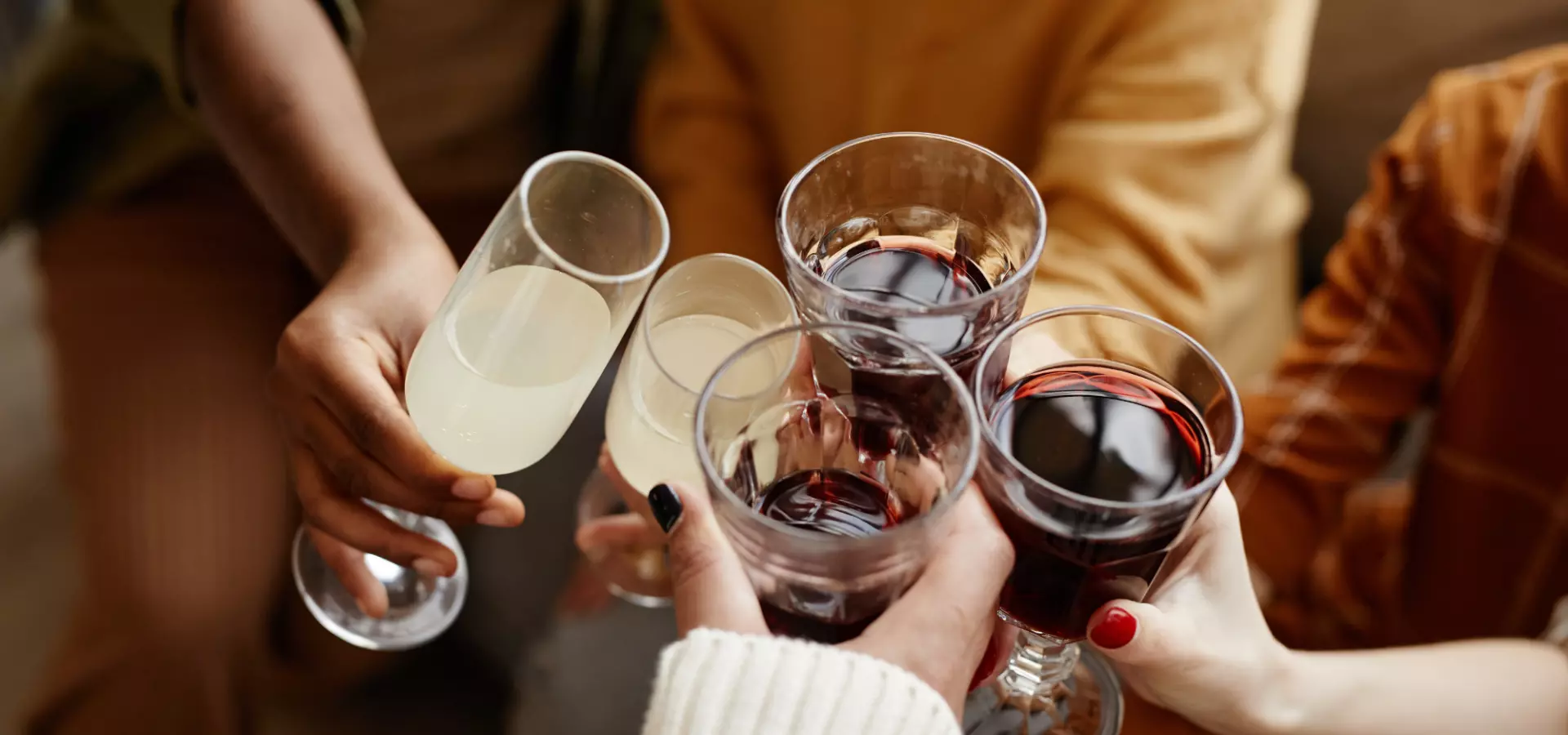 Close up on hands holding glasses of wine, cheering.