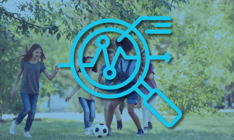 Group of children playing football in a park, with a magnifying glass icon on top to signify 'overview'.