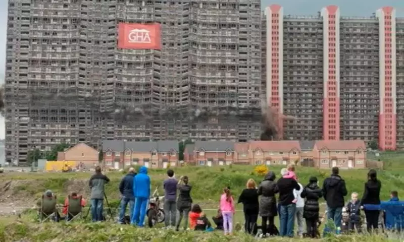 A crowd of people looking at the Red Road flats as they are being imploded.