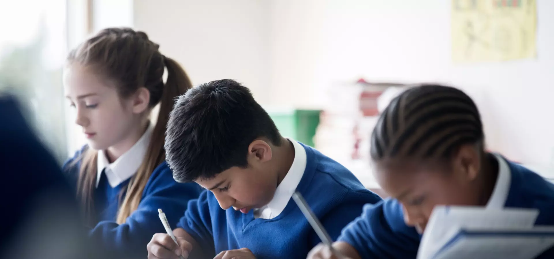 Three school children of different ethnicities working in class.