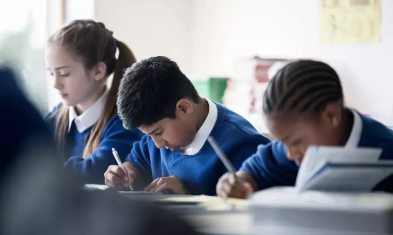 Three school children of different ethnicities working in class.